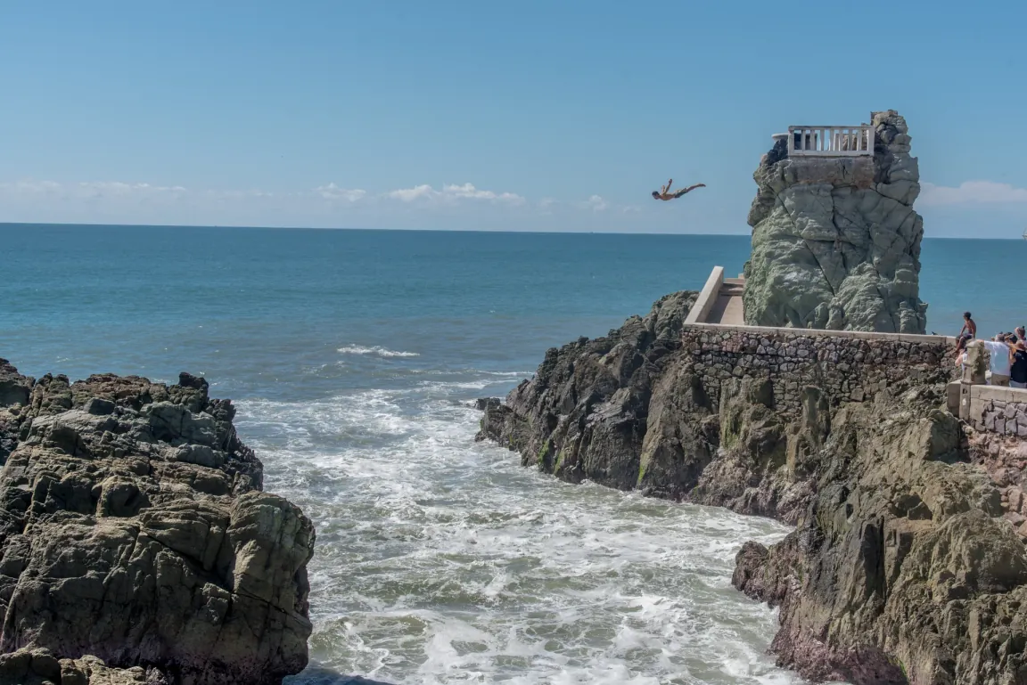 A cliff diver in mid-air over the rocks at the Mazatlán cliffs, the ocean waves breaking below